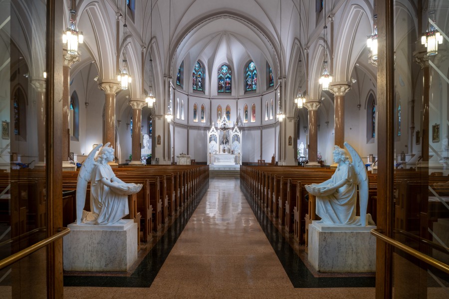 A wide-angle view of a majestic church interior featuring polished stone floors, high vaulted ceilings, and carved marble angel statues at the entrance of the nave.