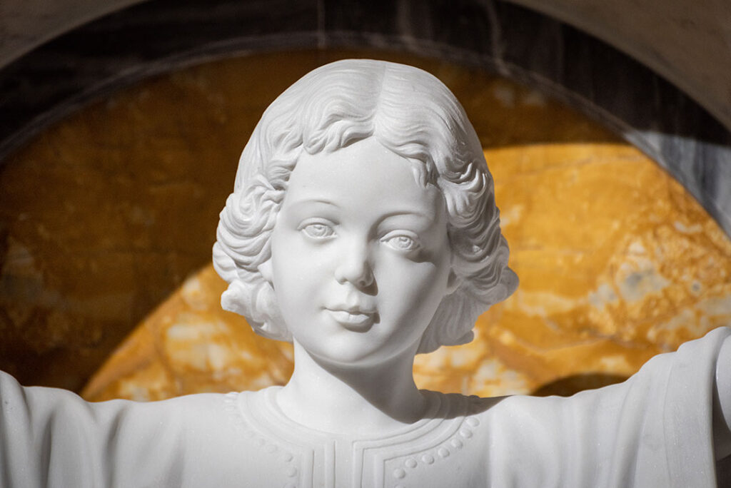 Close-up of a detailed white marble statue carving of a child with open arms in a modern church interior