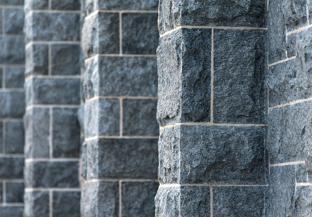Close-up of rugged, dark gray granite blocks with precise mortar joints, showcasing authentic historic stone restoration.