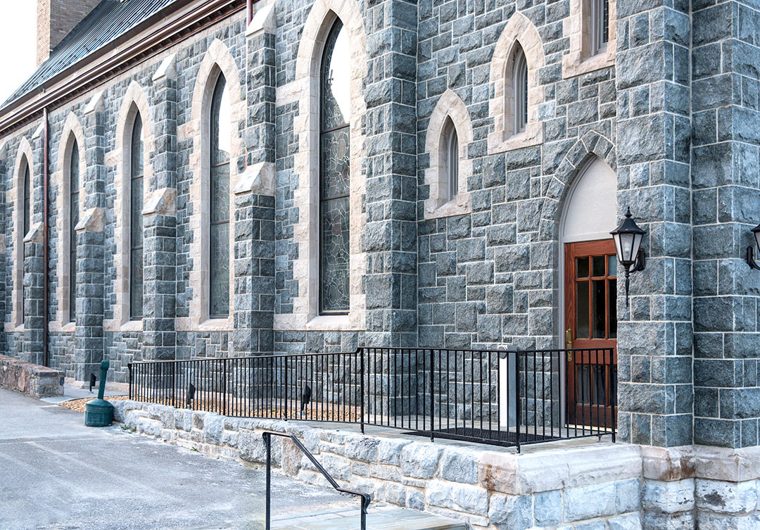 The exterior of a historic stone church featuring arched gothic windows and custom granite masonry restoration.