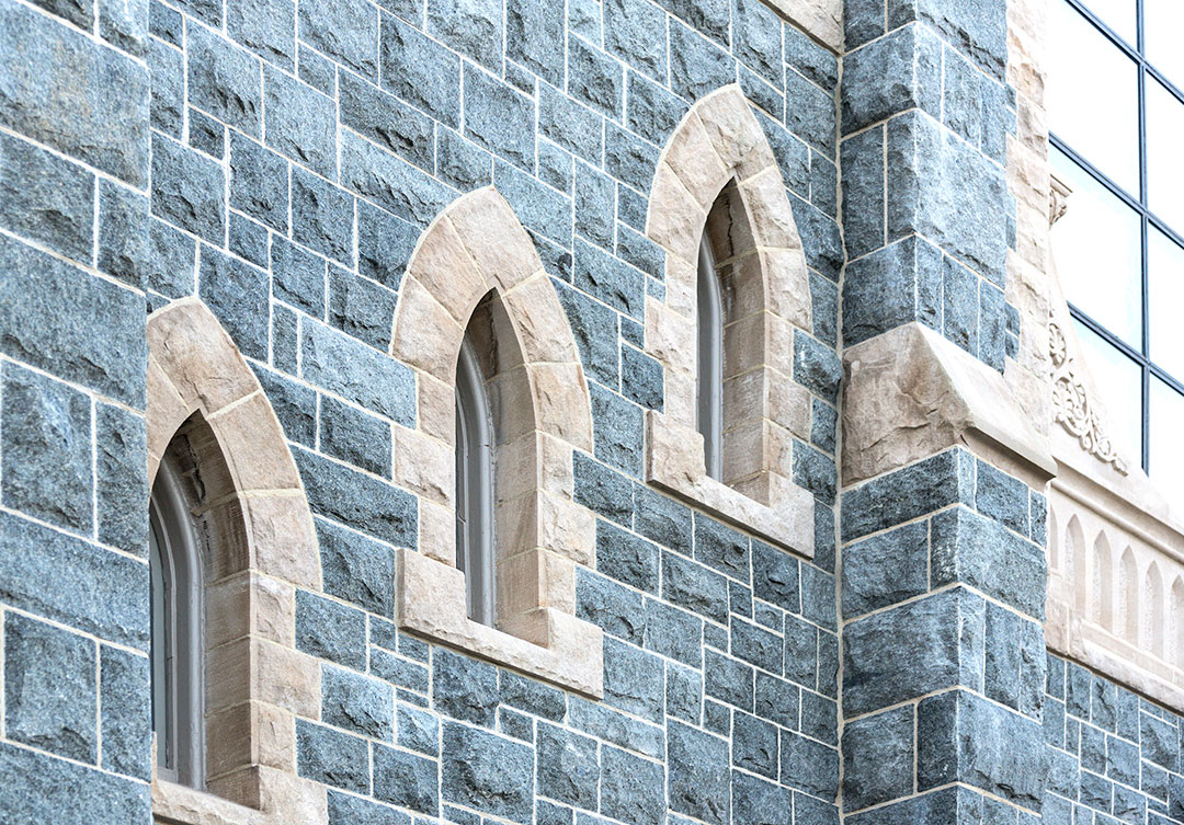 Detailed view of light-colored stone arched window surrounds integrated into a dark gray granite church façade.
