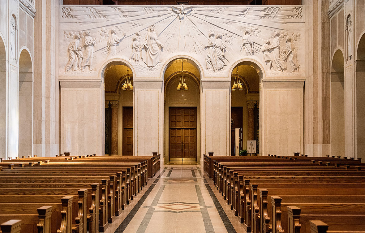 Detailed stone carving relief mural below a grand pipe organ and a circular stained glass rose window in a contemporary church cathedral