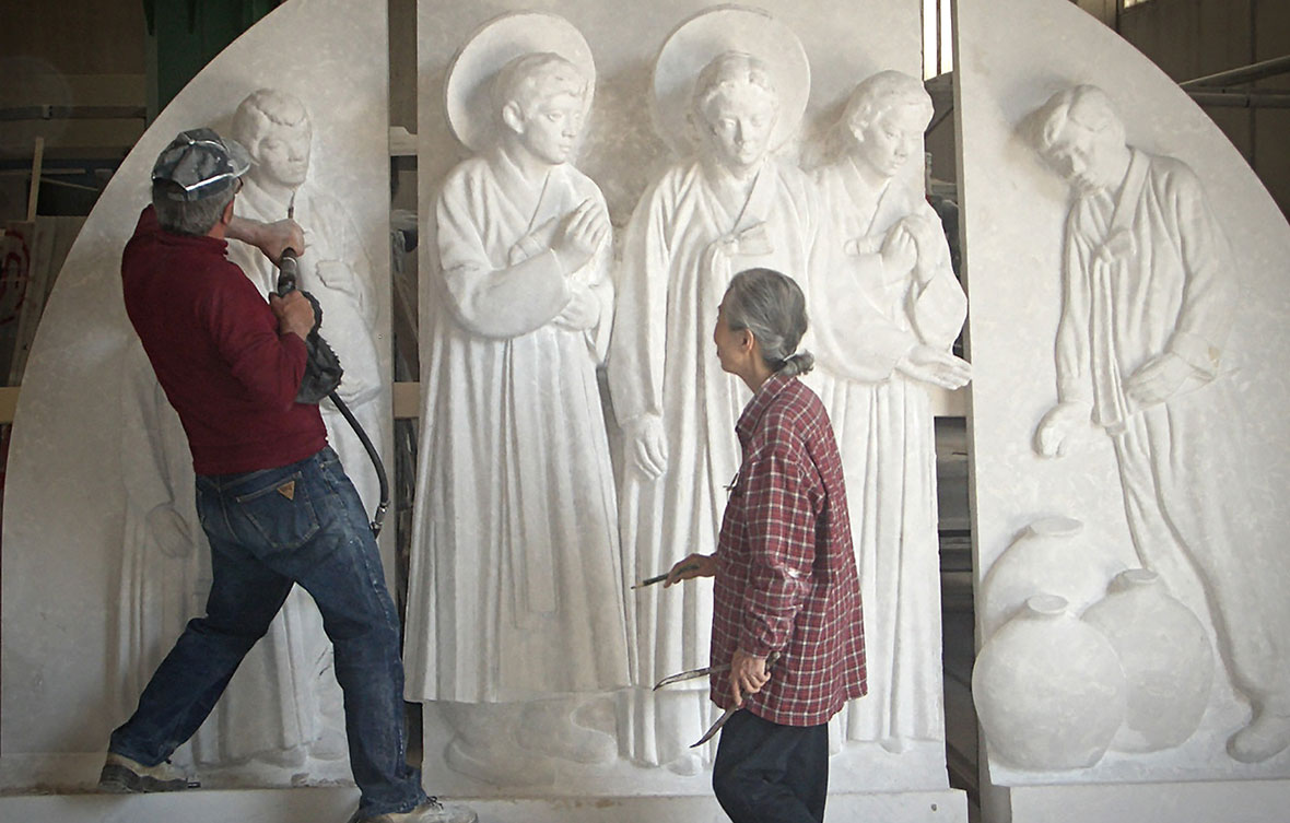 Close-up of skilled artisans and architects inspecting a white marble relief sculpture of a religious figure in a stone carving studio.