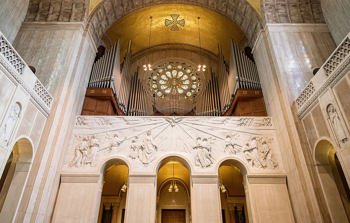 Modern church sanctuary featuring rows of wooden pews leading to a large, intricate stone-carved relief mural above the arches